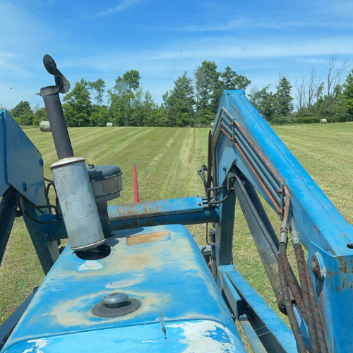 A driver seat view of a tractor cutting a pasture.